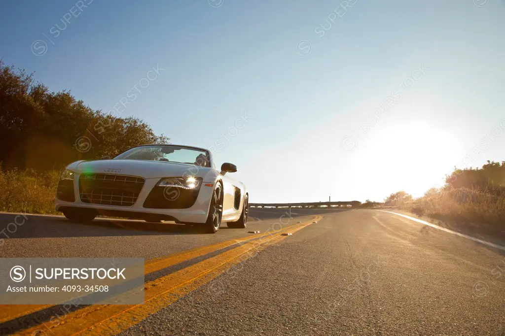 Low, static, front 3/4 view of a white 2012 Audi R8 Spyder on a winding, rural road.