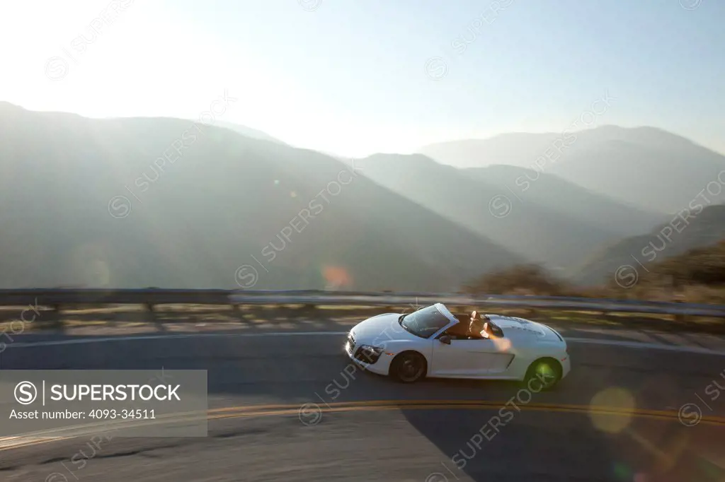 Overhead front 3/4 action of a white 2012 Audi R8 Spyder on a winding, rural, mountain road.