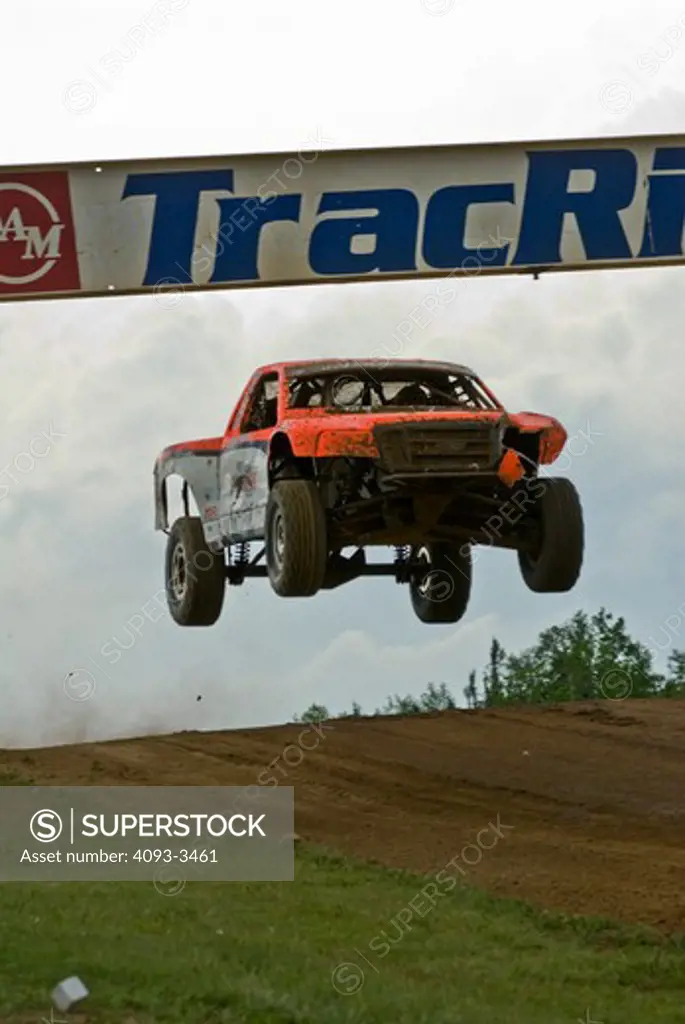 baja race truck going over a jump during a race with a sign above