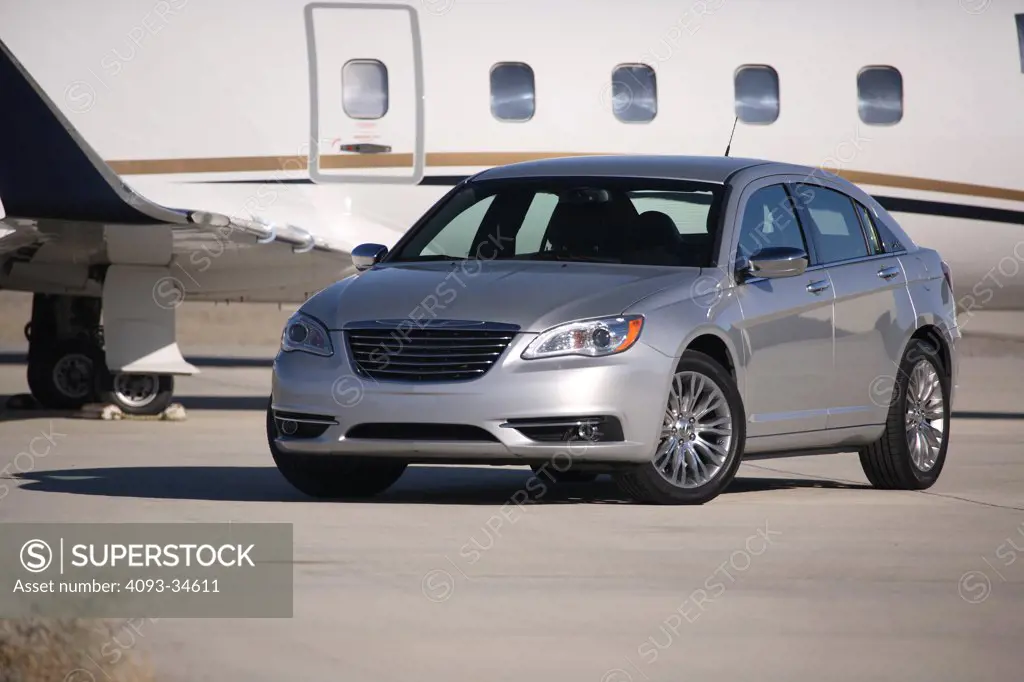 Front 3/4 static view of a silver 2012 Chrysler 200 parked in front of a Lear 60 jet.