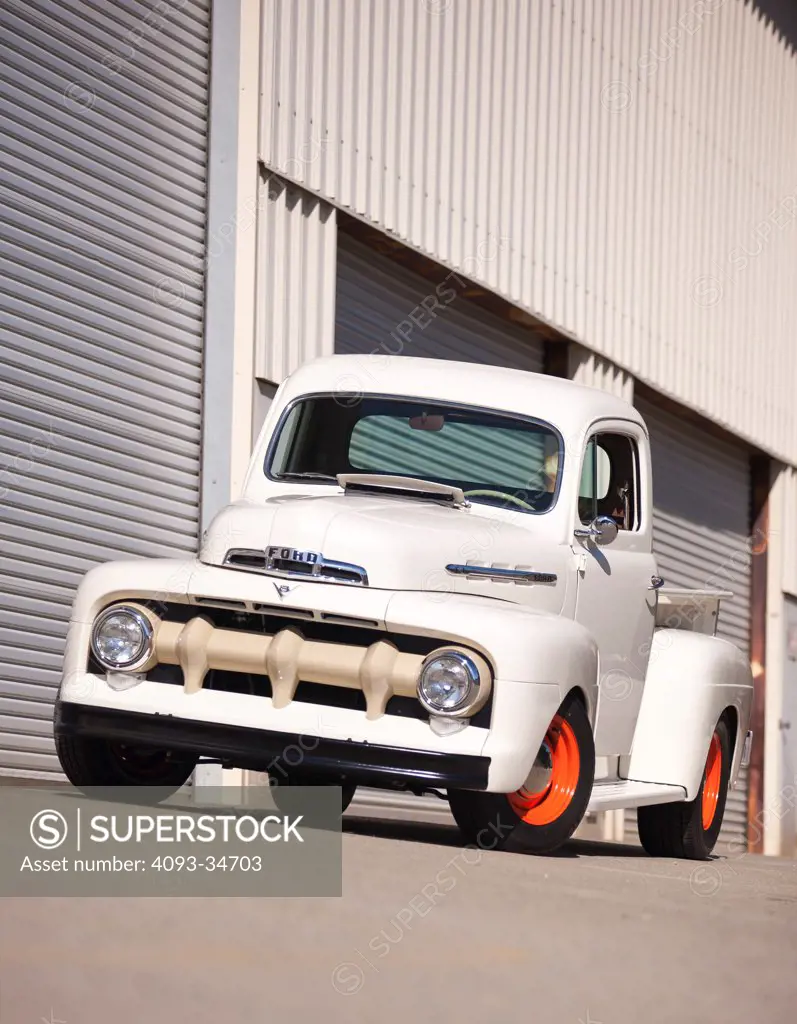 Front 3/4 static of a white 1952 Ford F-150 truck parked in front of a metal building.