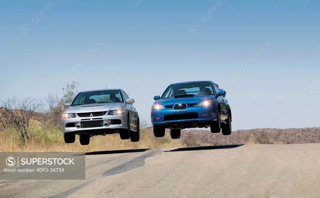 2006 Mitsubishi Evo IX MR and Subaru Impreza WRX STI on a jump on a rural road.