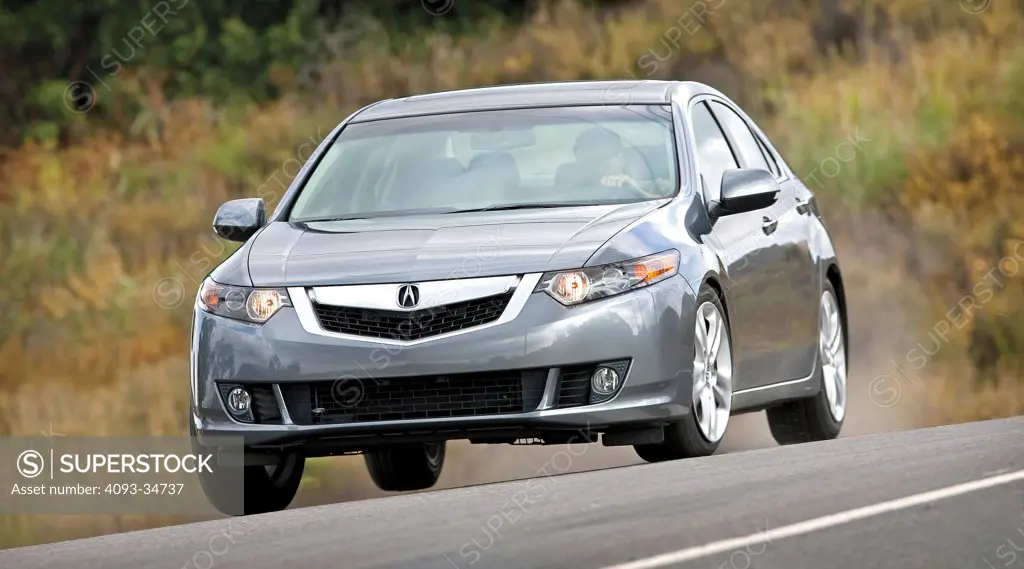 Front 3/4 action view of a 2010 Acura TSX on a rural road.
