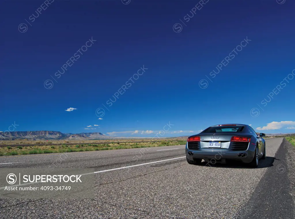 Static rear view of a 2010 Audi R8 parked on the side of a rural desert highway.