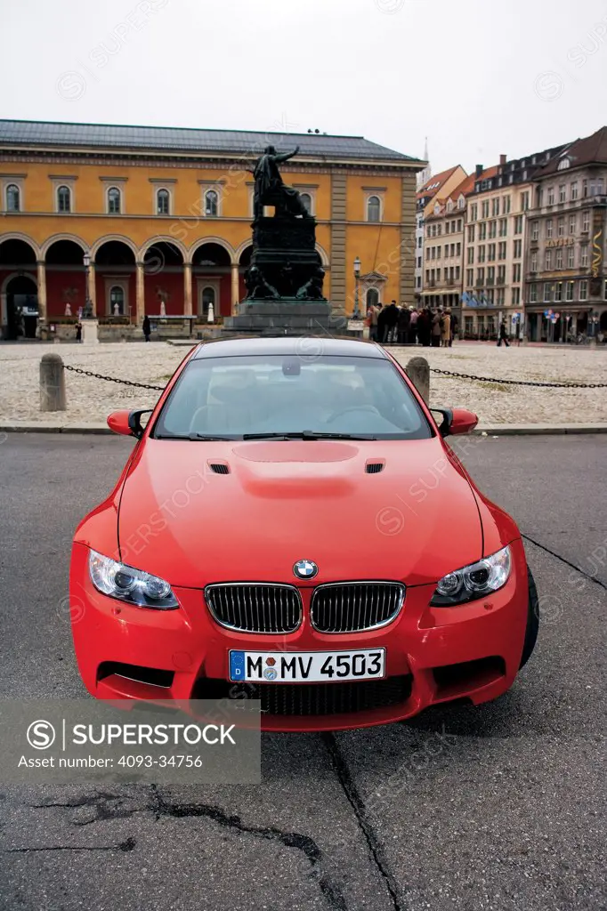Straight on nose view of a red 2008 BMW M3 parked in a city in Germany.