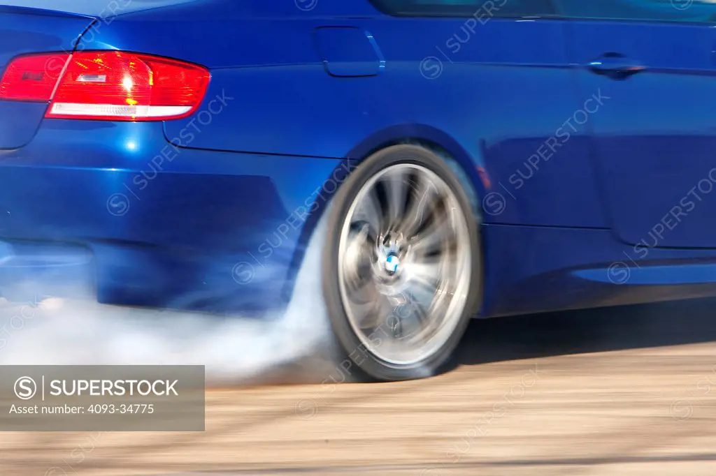 Detail action view of a blue 2010 BMW M3 doing a burnout and burning rubber with smoking tires.