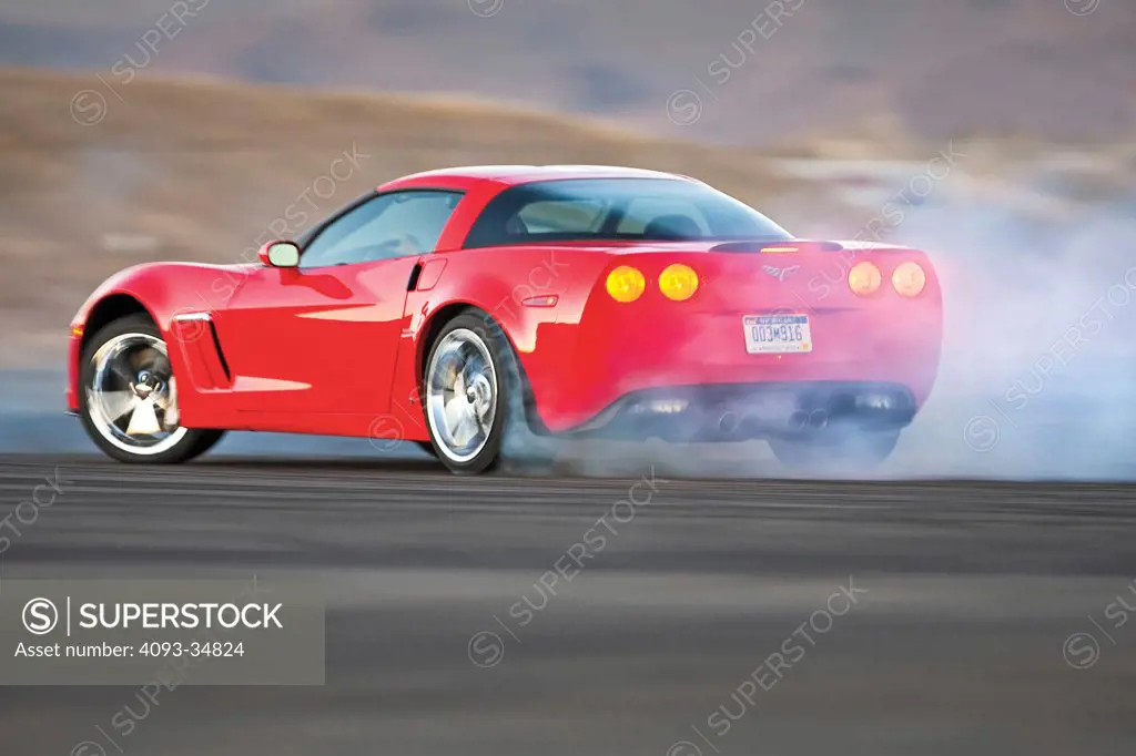 Rear 3/4 drifting action of a red 2010 Chevrolet Corvette Grand Sport. Burnout smoke.