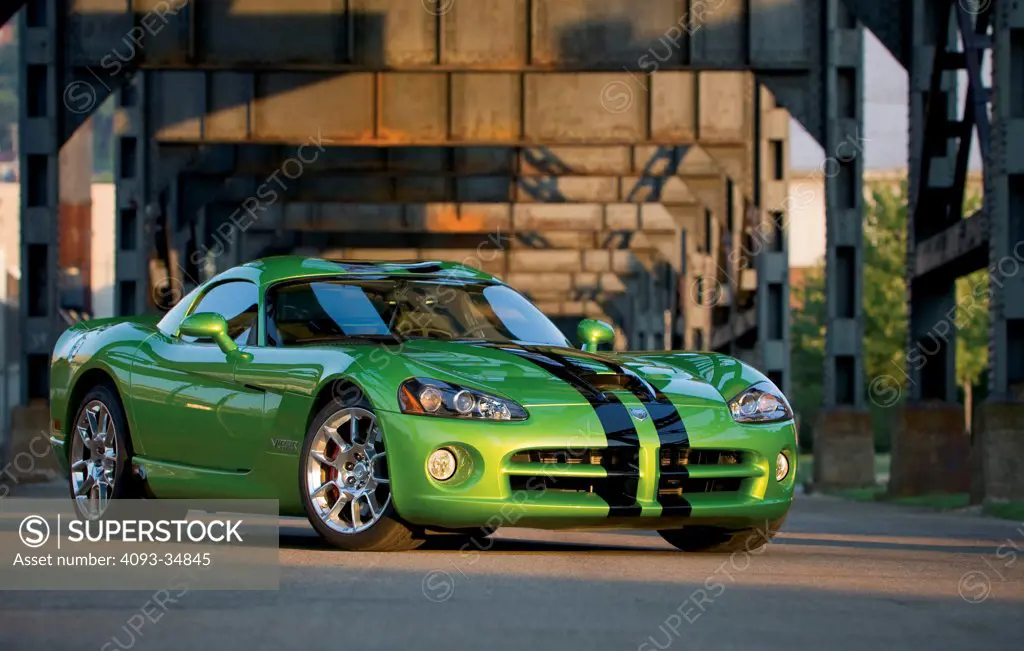 Static front 3/4 view of a green 2010 Dodge Viper SRT10 underneath a steel elevated railway.