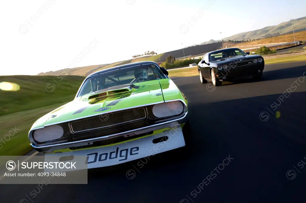 Straight on nose action view of a 1970 Trans Am Challenger and 2010 Dodge Challenger SRT8 on a race track.