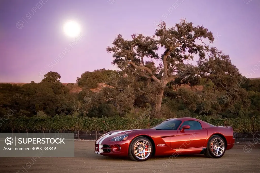 Static front 3/4 view of a red 2010 Dodge Viper SRT10 at dusk with the moon behind.