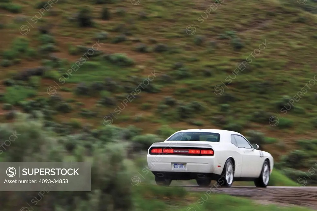 Rear 3/4 action view of a white 2010 Dodge Challenger on a rural mountain road.