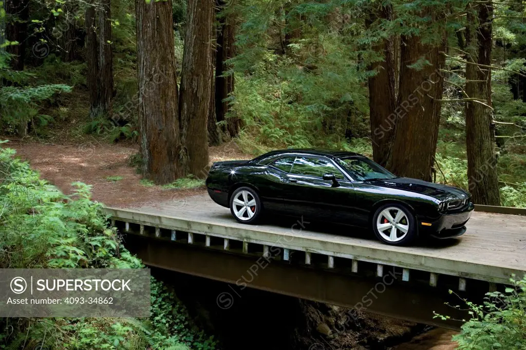 Front 3/4 static view of a black 2010 Dodge Challenger SRT8 on a rural mountain bridge.