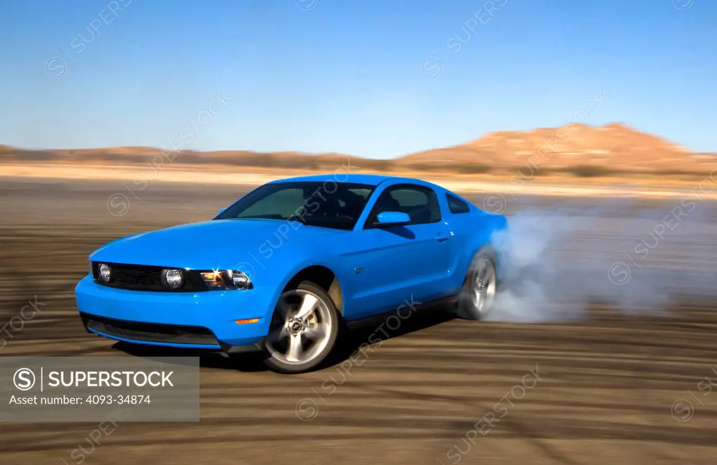 Front 3/4 drifting action of a blue 2010 Ford Mustang GT. Burnout and smoke.