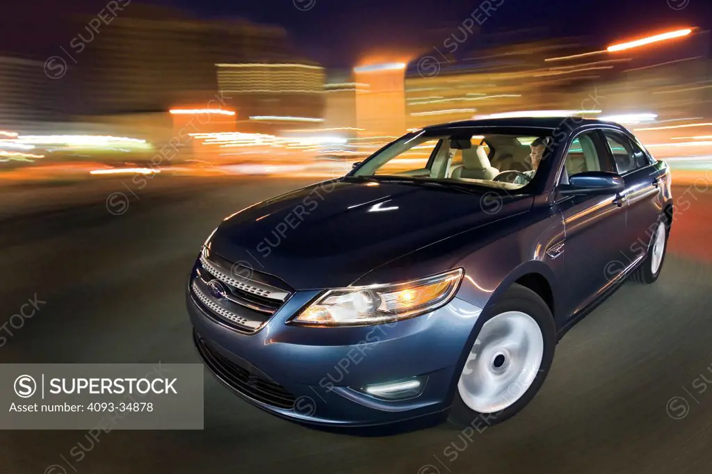 Front 3/4 action view of a blue 2010 Ford Taurus in the city at night.