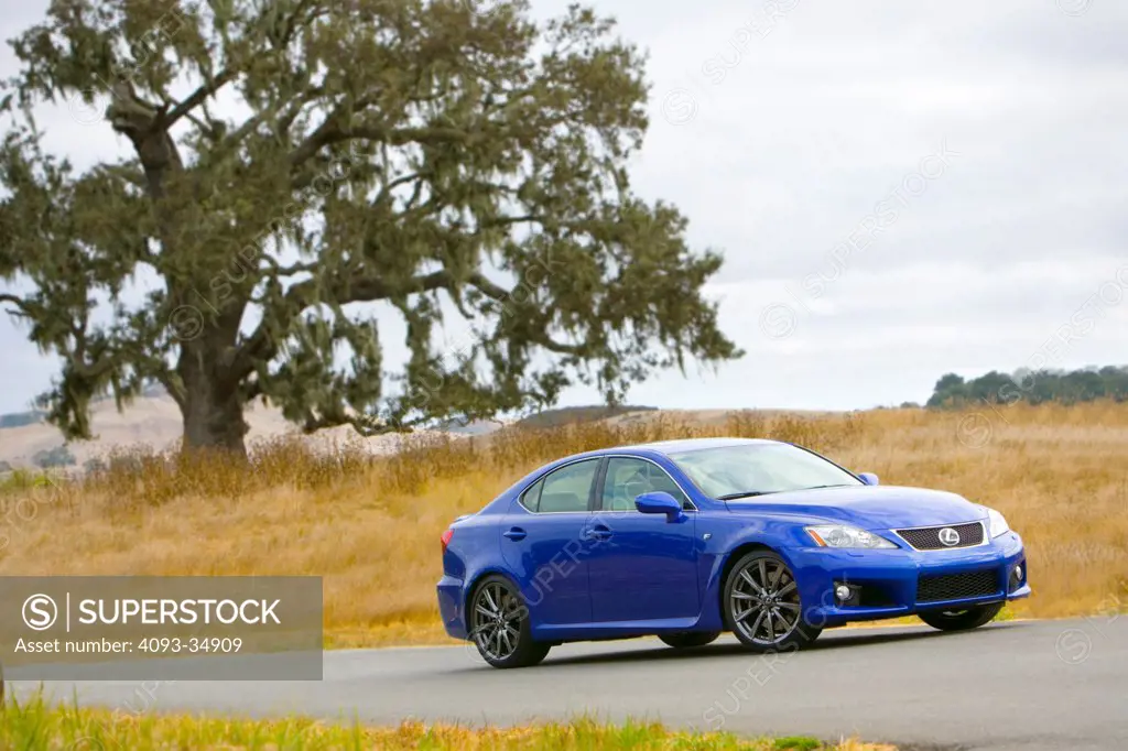 Front 3/4 static view of a 2010 Lexus IS-F on a rural mountain road near an oak tree.