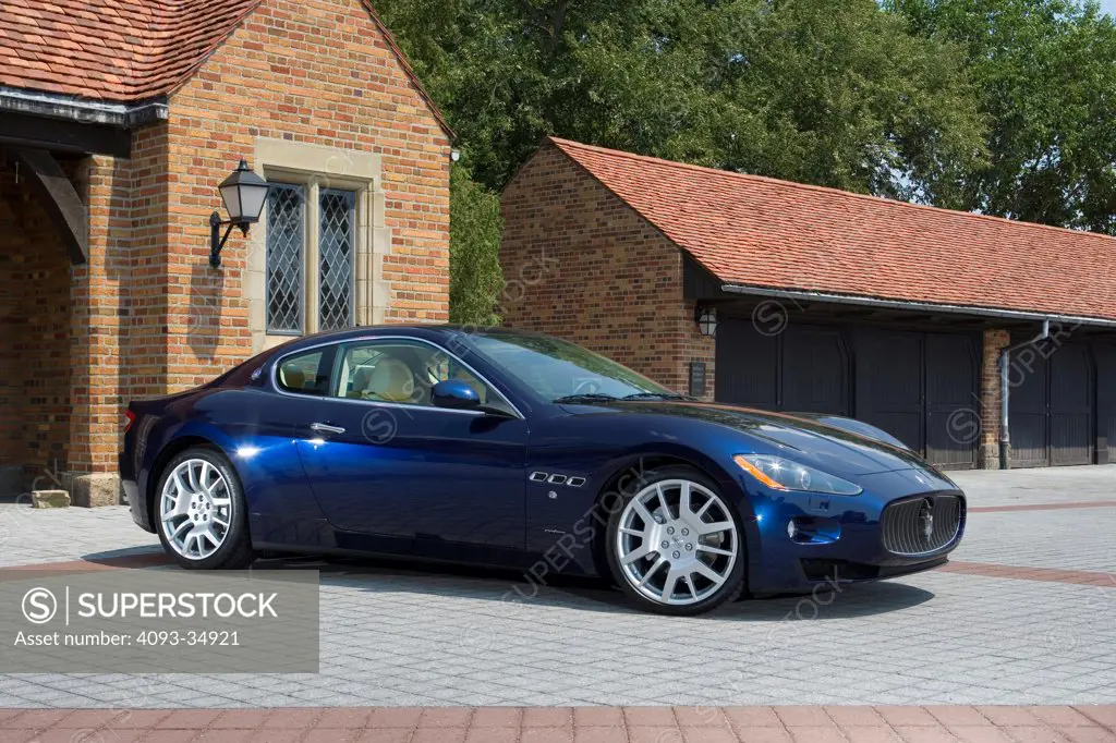 Front 3/4 static view of a blue 2010 Maserati GranTurismo in front of a private upscale garage.