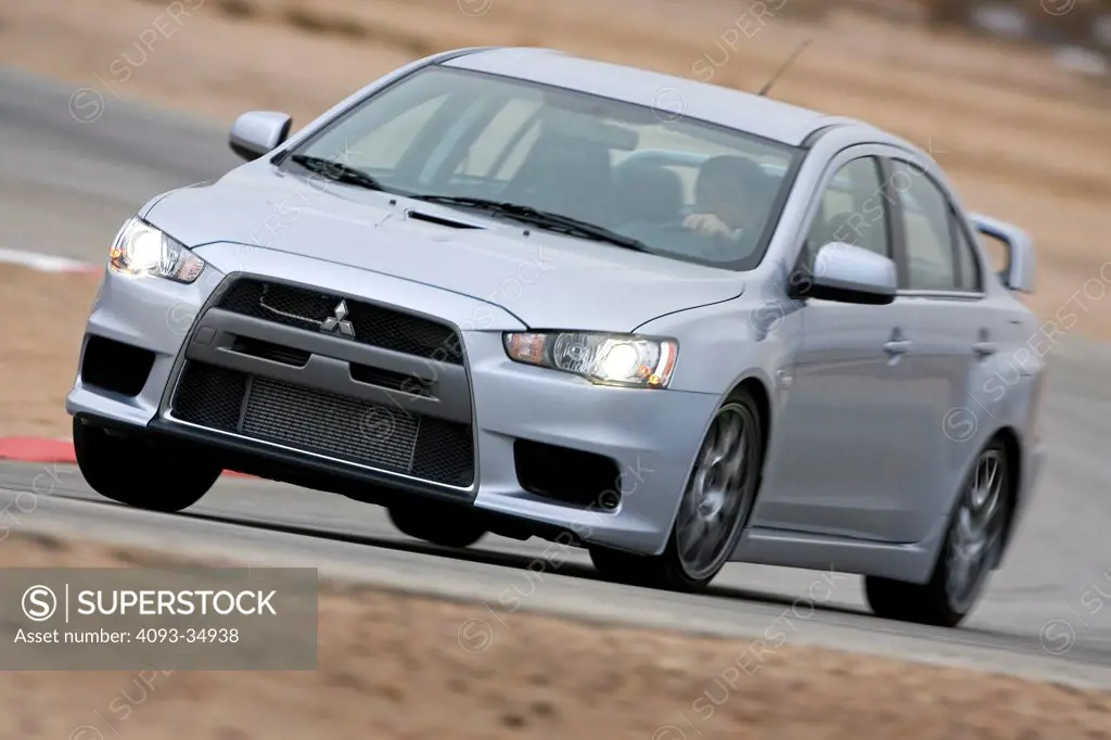 Front 3/4 action view of a silver 2009 Mitsubishi Lancer Evolution sports sedan on a race track.