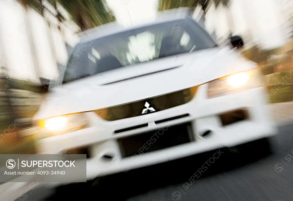 Straight on nose action view of a white 2010 Mitsubishi Lancer Evolution RS on a suburban road.