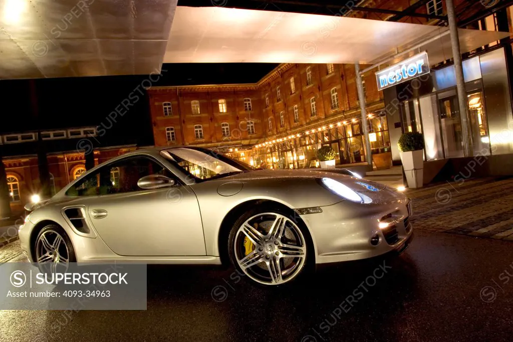 Front 3/4 static view of a silver 2010 Porsche 911 ( 997 series ) Turbo in a German village at night.