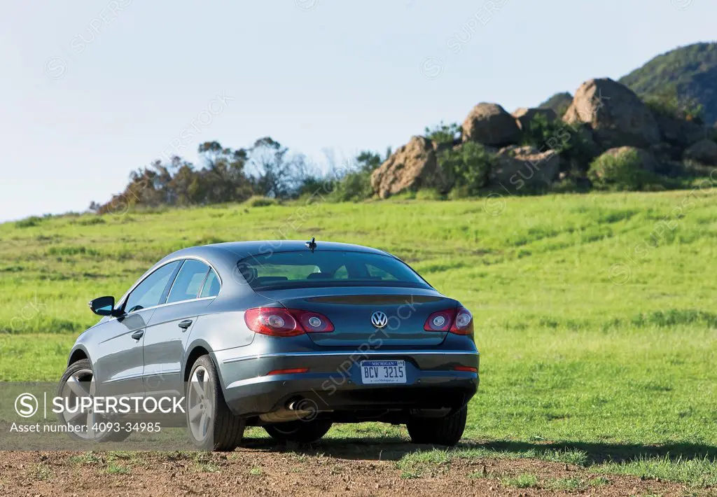 Rear 3/4 static view of a 2010 Volkswagen CC Passat on a rural dirt road with lots of green grass.