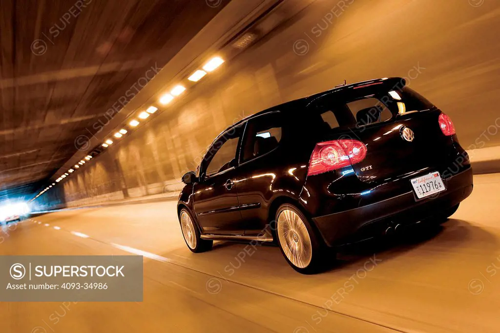 Rear 3/4 action view of a black Volkswagen GTI driving in a tunnel.