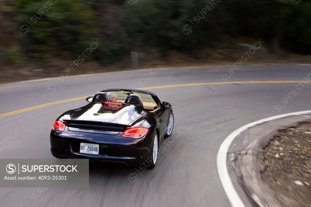 2010 Porsche Boxster Spyder driving around a tight corner on a rural mountain road, rear 3/4 action view