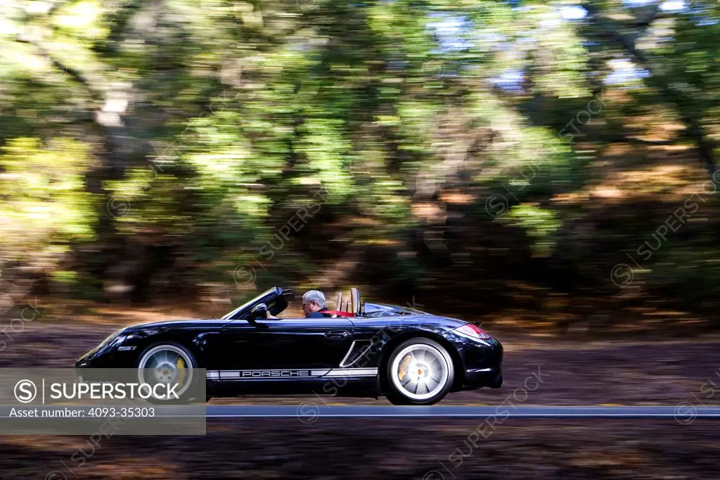 2010 Porsche Boxster Spyder driving fast on a rural mountain road, profile action view
