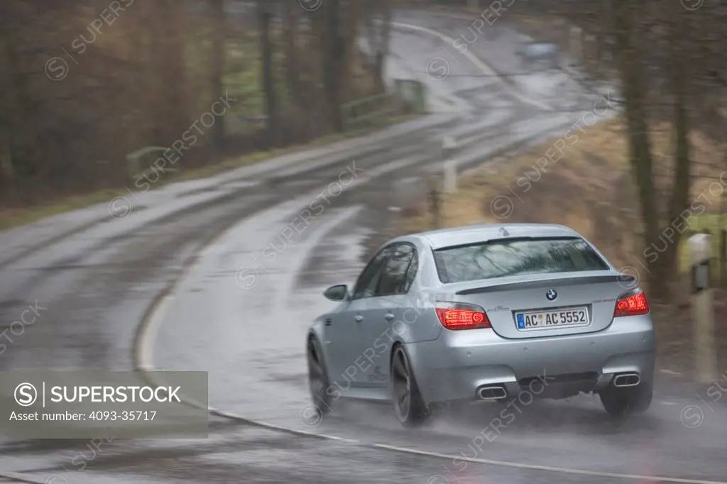 2006 AC Schnitzer ACS5 BMW M5 driving on a rural road in the rain, rear 3/4
