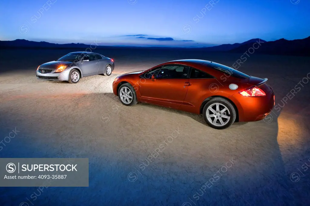 2007 Mitsubishi Eclipse GT and a silver 2008 Nissan Altima 3.5 SE parked on a dry lake bed at night