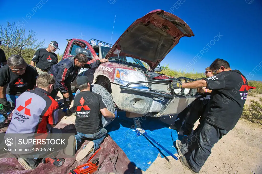Baja Race Truck off road racer racing mud and dirt pit crew working on car changing wheels tires up on a jack.