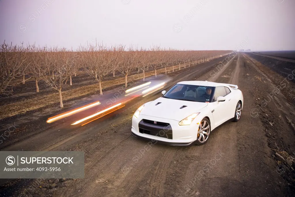 2008 Nissan GT-R GTR on a farm with two car passing by in the background blurred.  The Nissan GT-R is All-Wheel Drive with a twin-turbo 6 cylinder engine
