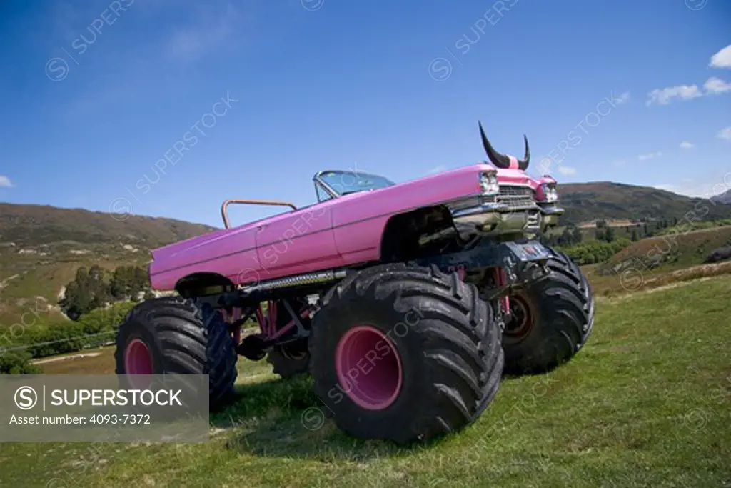 Classic pink convertible Cadillac on monster truck wheels, side view