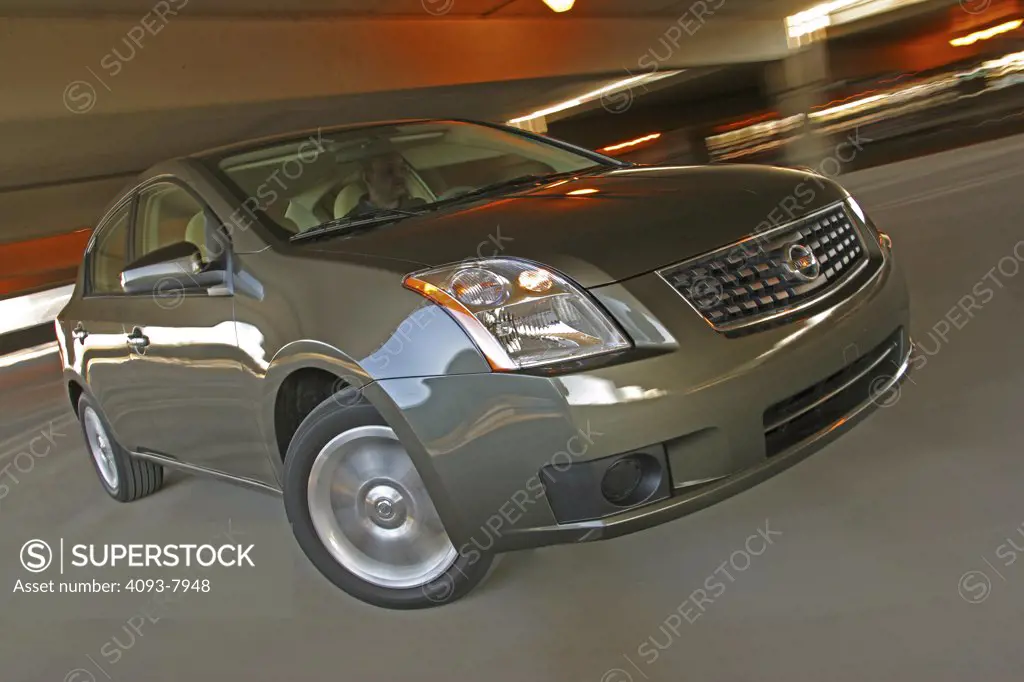 Front 3/4 action view of a 2007 green Nissan Sentra sedan. Inside a parking garage with lighting and turning.