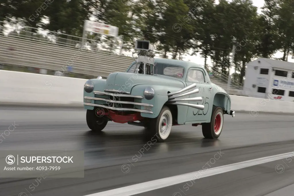 1949 Plymouth High & Mighty Dragcar. Front 3/4 action at the drag strip. The objective of the High and Mighty II was to re-create the legendary 50's drag racer -- the High & Mighty -- based on a 1949 Plymouth business coupe, and campaigned by the Ram Chargers in 1959. The car was a test bed for many revolutionary drag racing innovations still in use today. Baby blue aqu chrome speed track