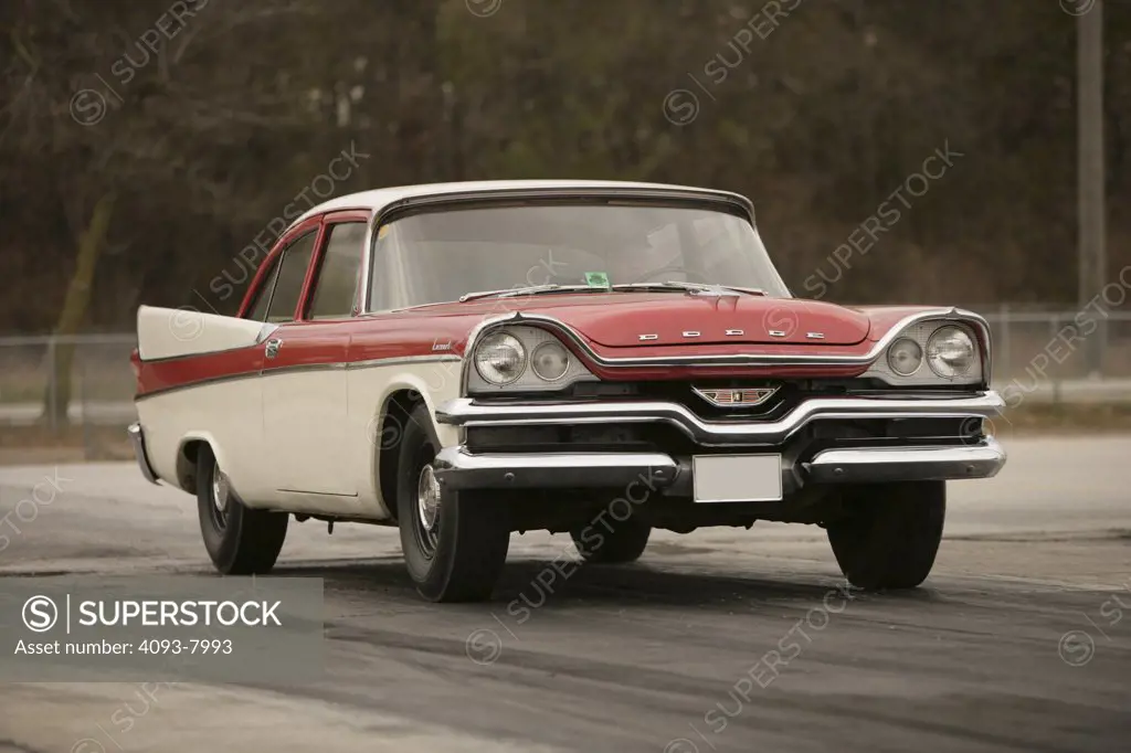 Front 3/4 action of a 1957 red & white Dodge Coronet Coupe with a 270 cubic inch V8 engine with dual rocker arms (The Hemi ).  at the starting line of a drag strip waiting reving getting ready about to start.