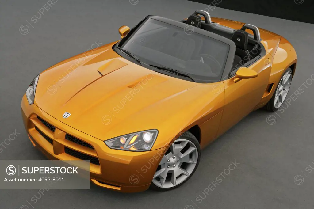 Front 3/4 overhead view of a Dodge Demon Convertible concept. Gold color inside parked viewing with backdrop