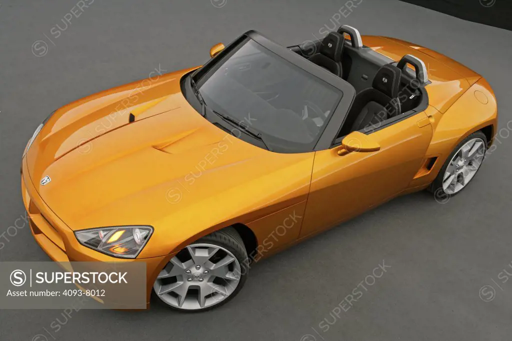Front 3/4 overhead view of a Dodge Demon Convertible concept. Gold color inside parked viewing with backdrop