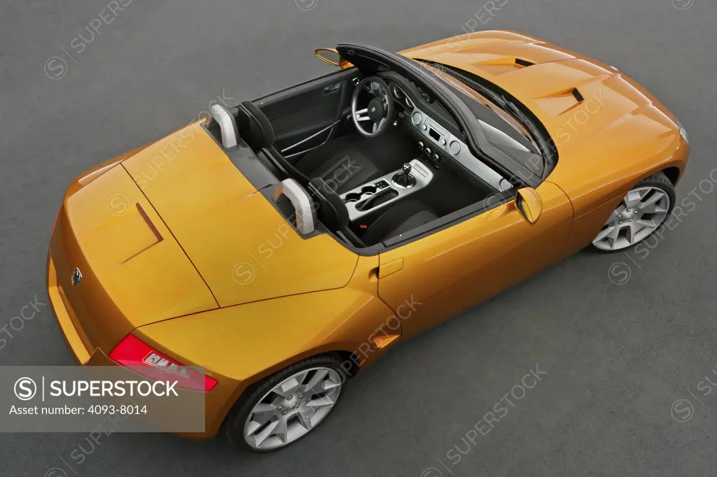 Rear 3/4 overhead view of a Dodge Demon Convertible concept. Gold color inside parked viewing with backdrop