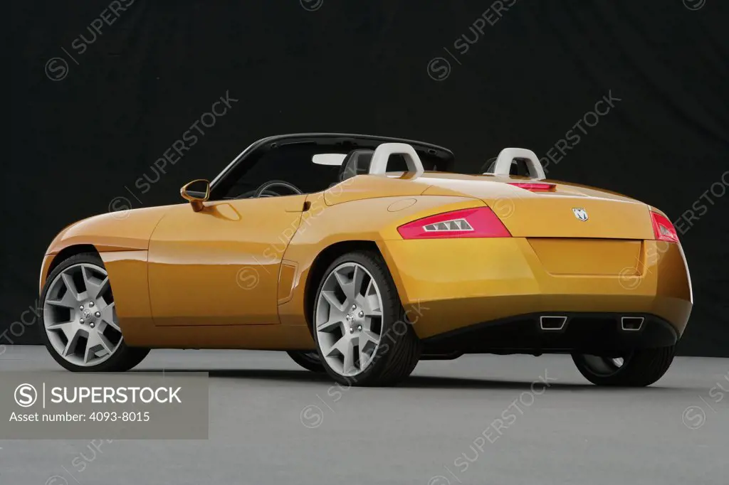 Rear 3/4 view of a Dodge Demon Convertible concept. Gold color inside parked viewing with backdrop