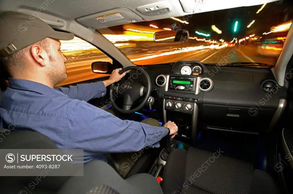 a man driving a car at night.  From inside looking out at the blurred lights