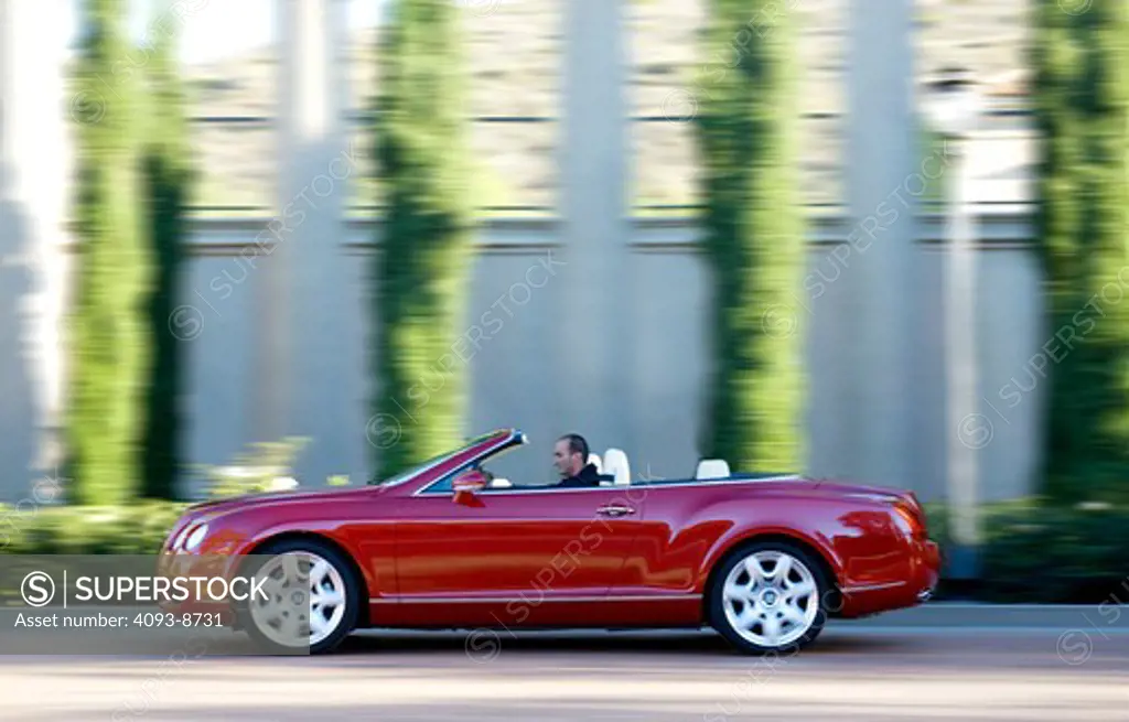 2009 Red Bentley Continental GTC driving along road, side view