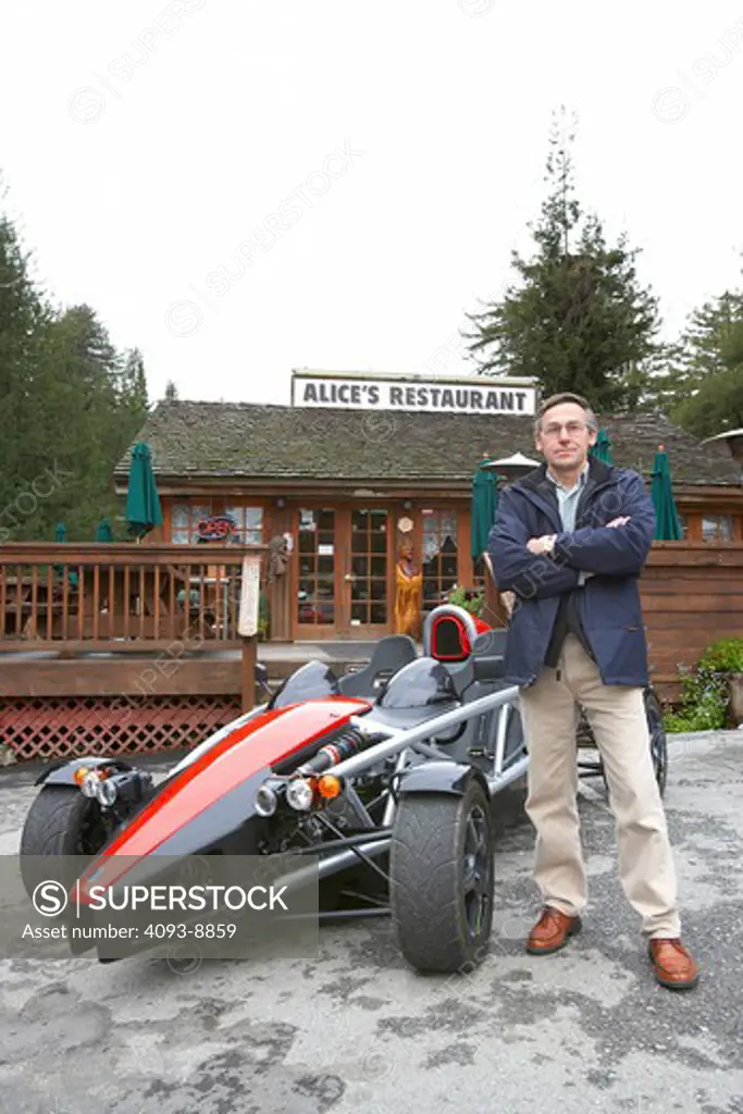 Wrightspeed x1 prototype 2005 with Ian Wright standing next to it in front of Alice's Restaurant.  Ian Wright is the inventor of the Wrightspeed x1 prototype. 0-60 ~ 3.0 seconds; Standing quarter mile ~11.5 seconds; Top speed 112mph (electronically limited); Range >100 miles in urban use; Charger: onboard conductive. Input 100-250V 50 or 60 Hz. Current: user adjustable up to 80A; Energy consumption 200 WHr/mile in urban use, equivalent to 170 mpg (33,705 WHr/gallon)