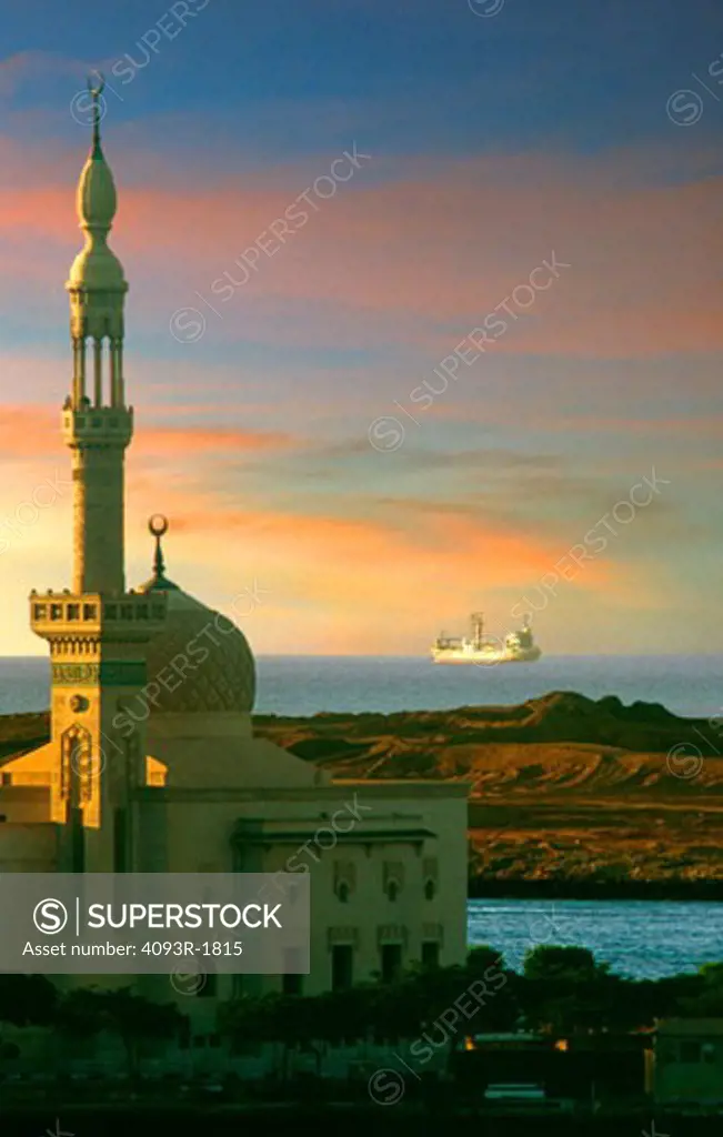 A cargo ship leaving the Suez Canal with a mosque in the foreground. Egypt, Africa. Middle East