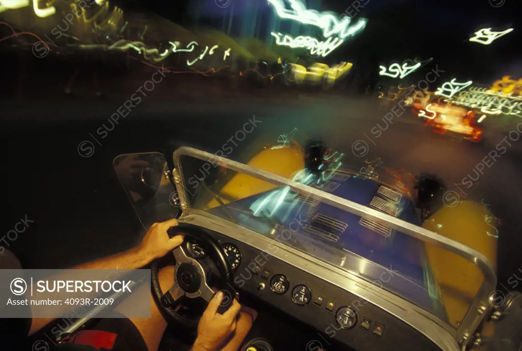 interior Lotus Super Seven 1970s yellow dashboard gauges hands steering wheel motion city lights street