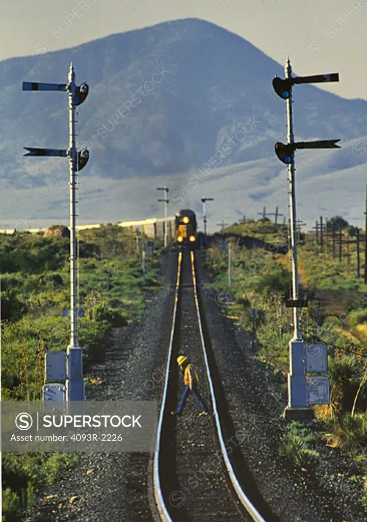 railroad worker crossing tracks ahead of an advancing freight train.