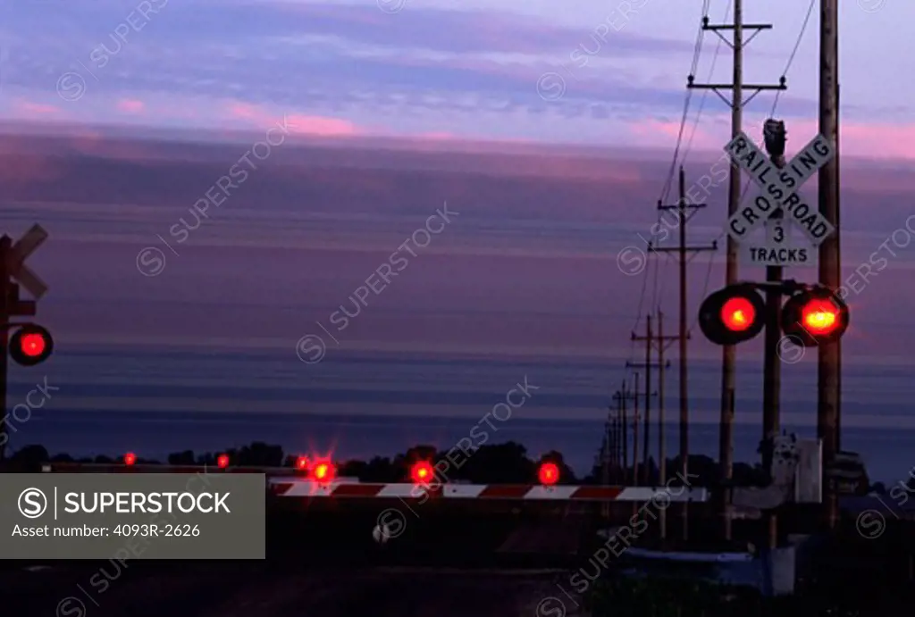 Railroad crossing signal / guard with lights on and gate down at sunset.