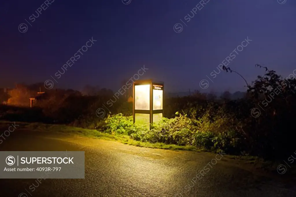 A phone booth on the side of an empty road at night.