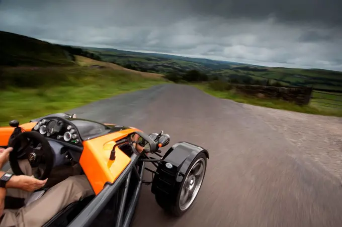 Overhead POV action of an orange 2010 SDR Exoskeleton sports car on a rural road in England UK.