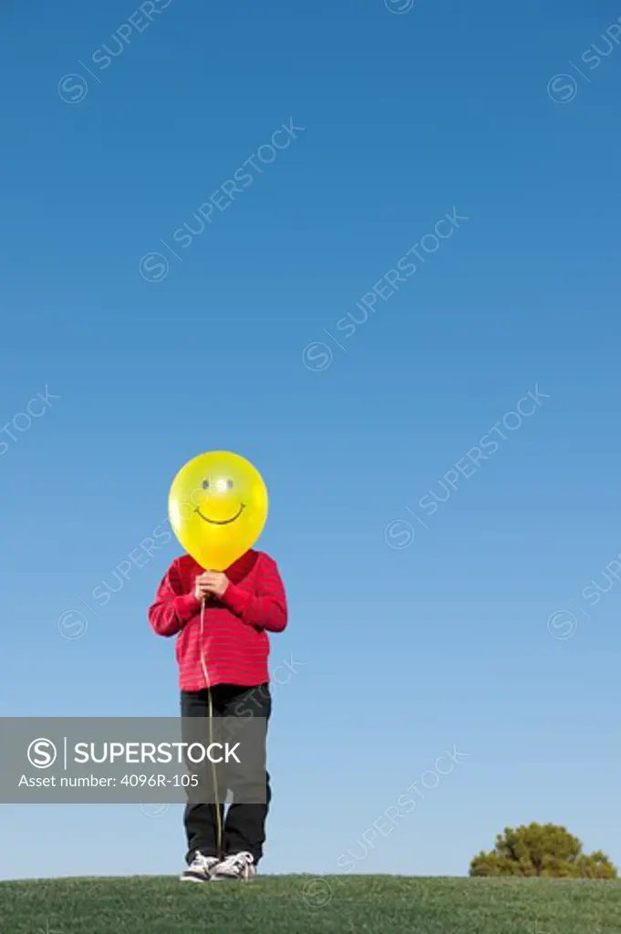 Boy holding a smiley face balloon in front of his face