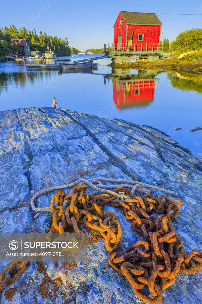 Rusty chain on a rock with a boat shed in the background, Stonehurst East, Nova Scotia, Canada